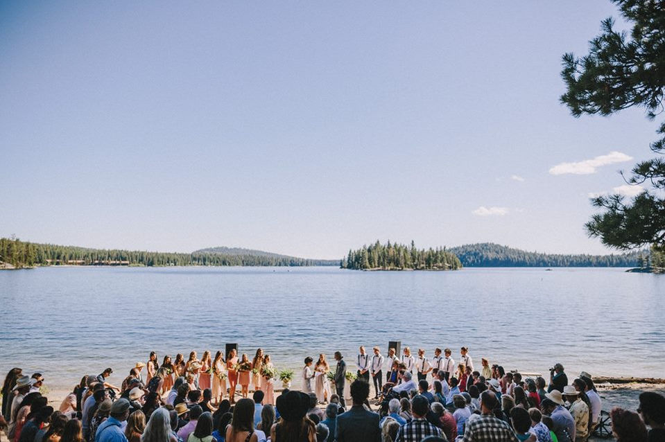 Wedding ceremony and guests on beach with view of lake and islands behind.