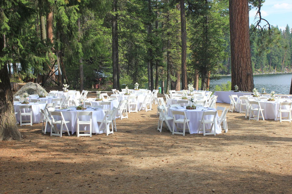 Outdoor reception area set with white chairs surrounding tables with white tablecloths.